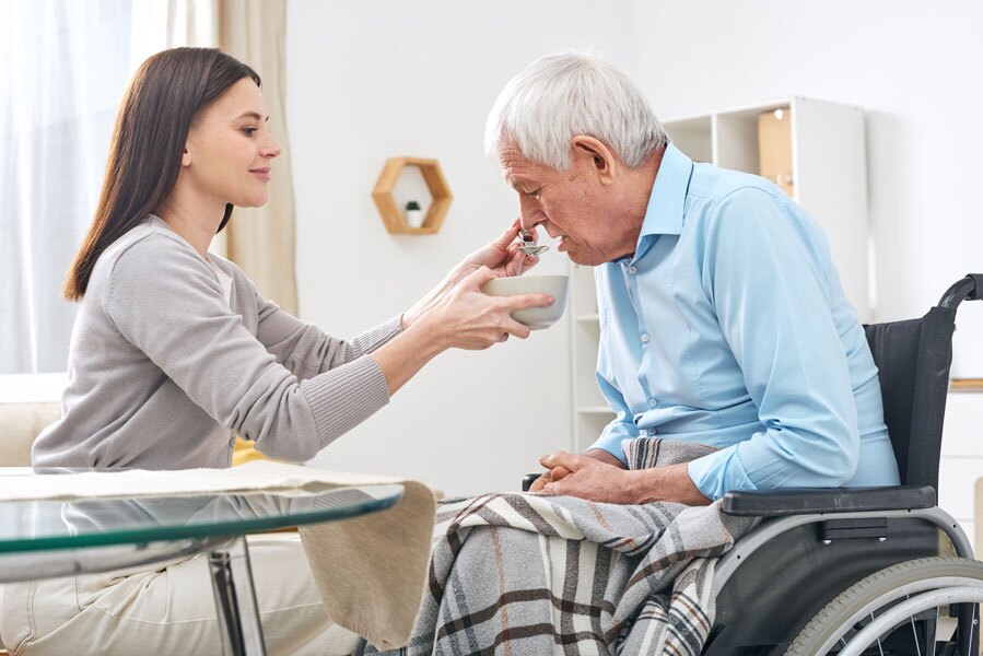 Caregiver helping a senior man in a wheelchair with his meal